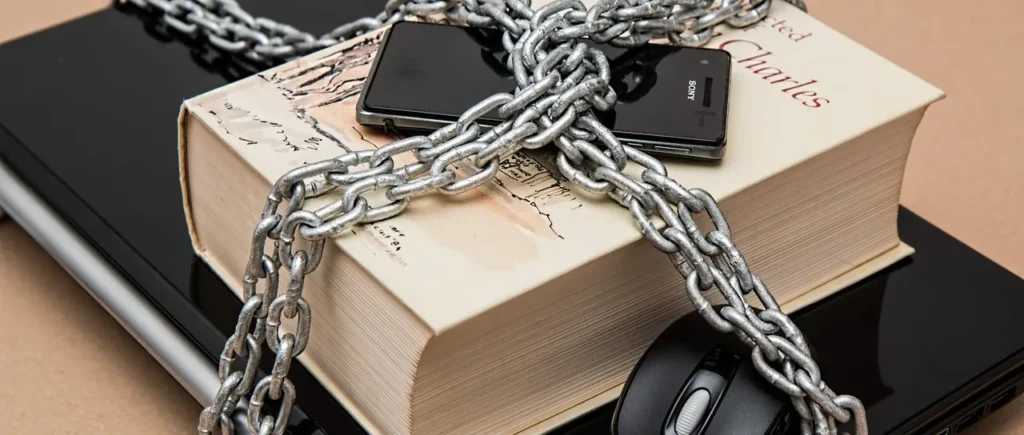 책과 노트북, 스마트폰 등 전자기기가 쇠사슬에 묶여 있는 이미지. 이는 과거 문재인 정부의 30회가 넘는 복잡한 부동산 규제와 수요 억제 정책으로 인한 시장의 경직성을 상징합니다.